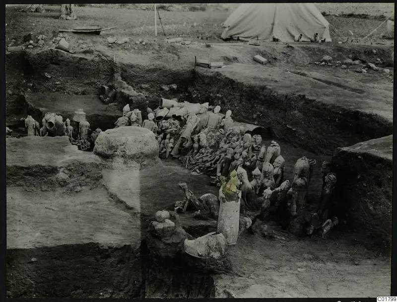 In situ finds in an excavation trench at Ayia Irini, with figurines and vessels and a tent beyond.