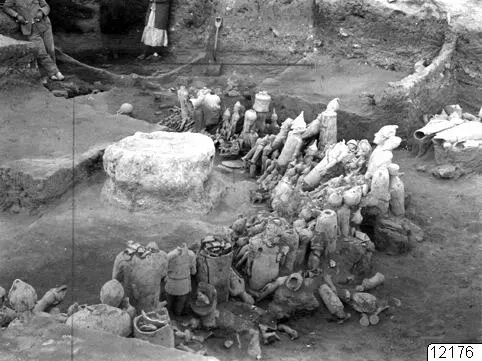 Excavation at Ayia Irini with many broken sculptures and large vessels lying in the soil around a stone drum.