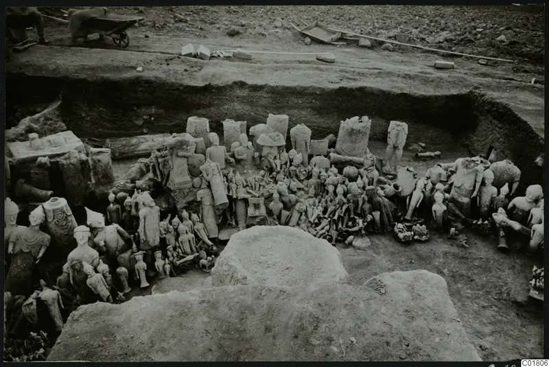 Excavated trench at Ayia Irini with a dense heap of clay figurines and sculpture fragments lying among stone blocks