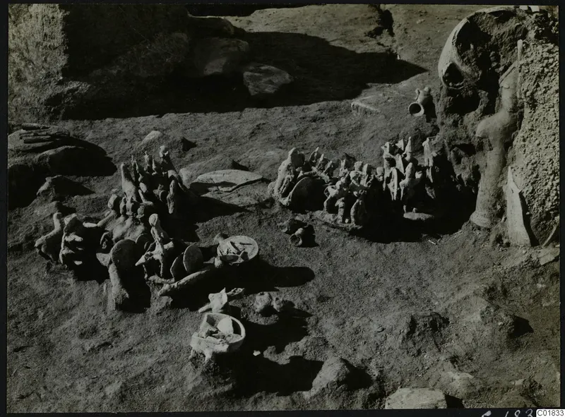 Clay figurines and a bowl lying in situ in excavated ground at Ayia Irini