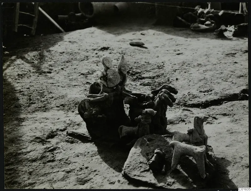 Terracotta figurines and animal figures lying in situ on a dusty excavation floor at Ayia Irini.