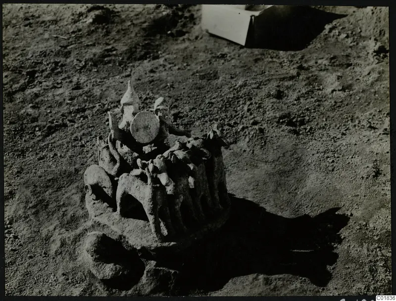 Modelled clay object with animal forms and a round disc on top, lying in excavation soil at Ayia Irini