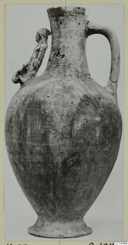 Pottery jug with a broken neck, a strap handle on the right and a modelled handle on the left, on a grey background