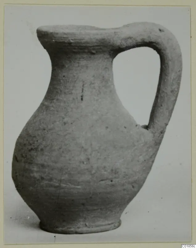 Pottery jug with a single loop handle and a flat rim, photographed on a plain background.