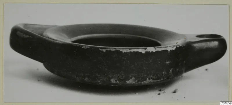 Black glazed two-handled bowl seen from the side against a pale background