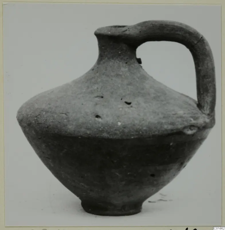 Pottery jug with a single handle and a narrow neck, photographed against a plain background.