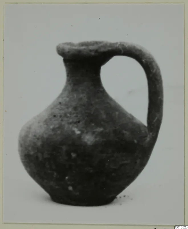 Black Slip juglet from Marion with a single strap handle, shown on a pale surface.