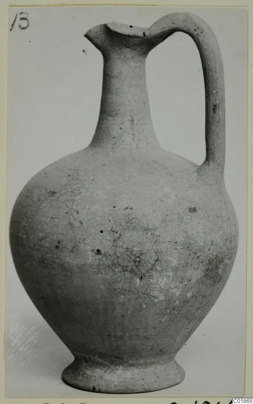 Plain white pottery jug with a tall neck, single loop handle and ring base, photographed against a grey backdrop.
