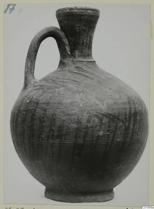 Pottery jug with a single handle, a flared neck and dark vertical strokes on its body