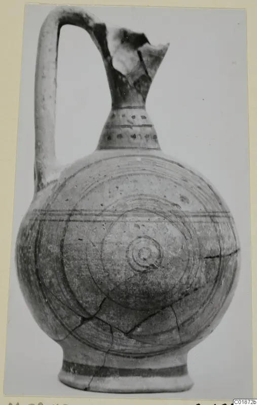 Round-bodied jug with a broken upper neck and handle, decorated with concentric circles and bands, photographed on a plain background.