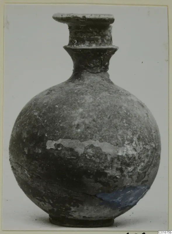 Round-bodied jug with a tall flared neck and rim, dark worn surface, shown against a plain background.