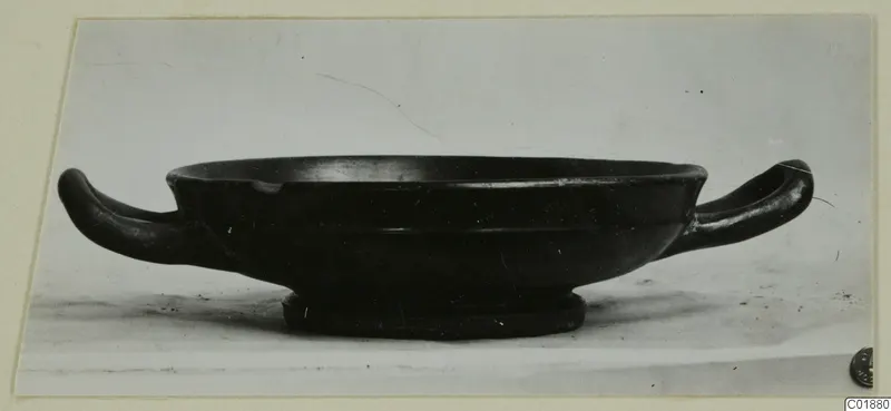 Black glazed two-handled kantharos, side view, on a pale surface