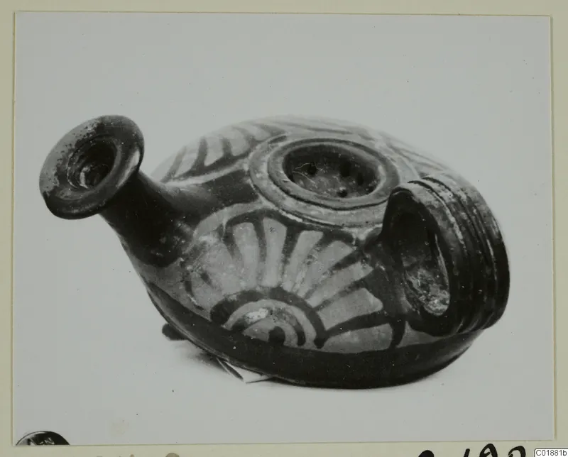 Strainer-spouted vessel with a flared spout, a perforated top opening and a ribbed handle, painted with radiating bands.