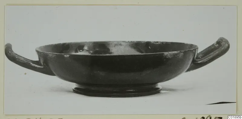 Black glazed bowl with two horizontal handles and a low foot, photographed on a plain background.