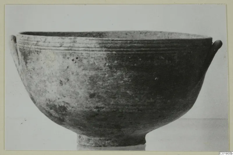 Pottery bowl with a ring foot and two small handles on the rim, photographed against a plain background