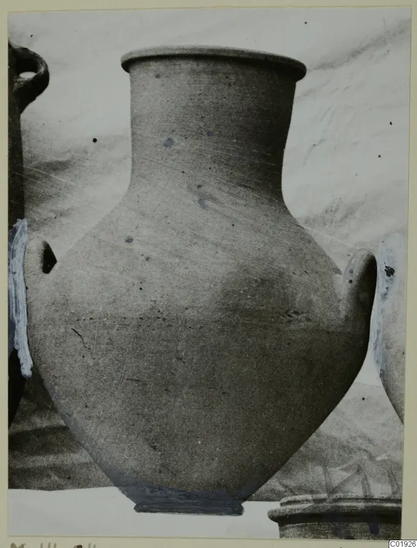 Large plain pottery vessel with two handles and a flat rim, photographed against a pale cloth backdrop