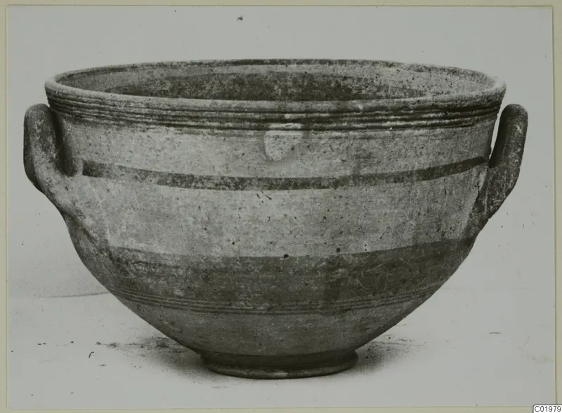 Pottery bowl with two loop handles and horizontal painted bands, photographed on a plain surface
