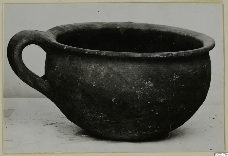 Coarse ware cup with a single loop handle, photographed on a pale surface.
