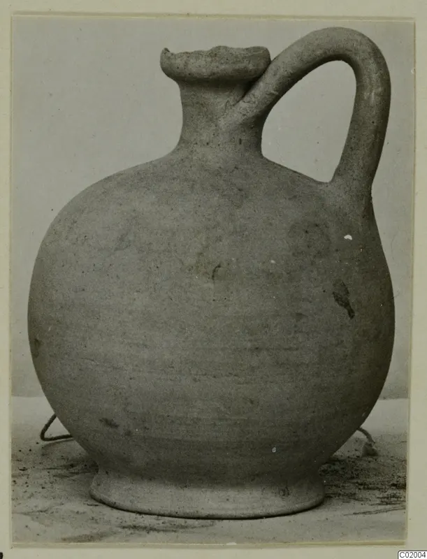 Pottery jug with a round body, a single loop handle and a short collar neck, photographed on a plain surface.