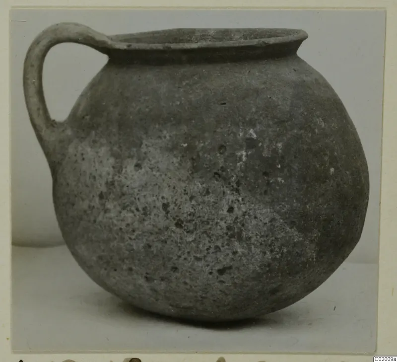 Coarse ware jug with a single loop handle and a rounded body, photographed against a plain background.