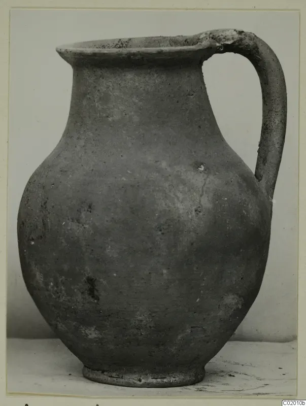 Plain pottery jug with a single loop handle, shown against a pale backdrop.