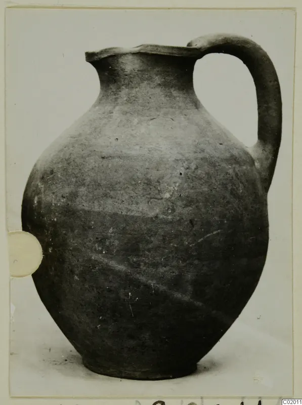 Pottery jug from Vouni with one handle and a plain grey-brown surface, photographed on a pale background.