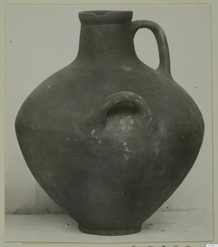 Coarse ware jug with a loop handle and a small loop lug on the body, photographed against a plain background.