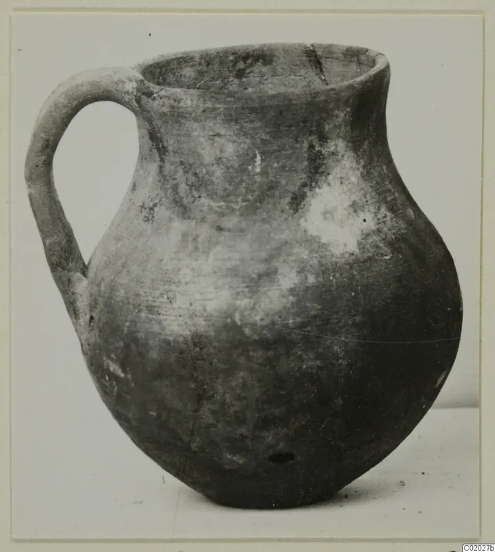 Coarse ware jug with a strap handle and rounded body, photographed on a plain surface