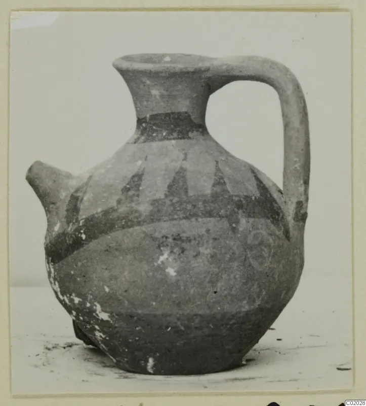 Pottery White Painted VI jug with a spout, strap handle and dark painted bands, shown on a plain surface