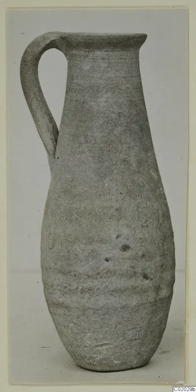Plain pottery jug with a single loop handle and a tall, narrow neck, photographed upright on a plain background.