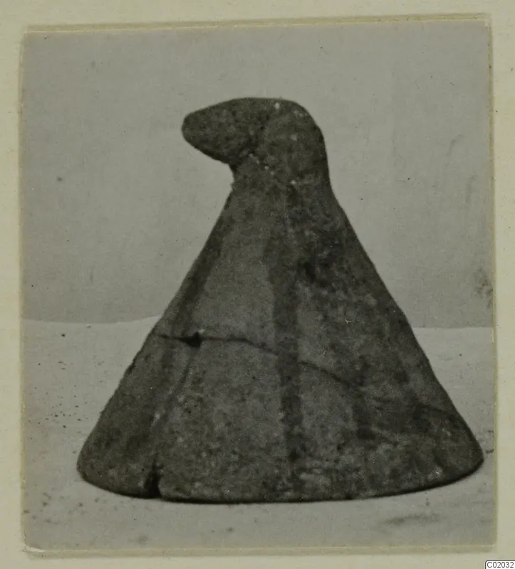 Cone-shaped object with a rounded knob at the top, photographed on a pale surface against a plain backdrop