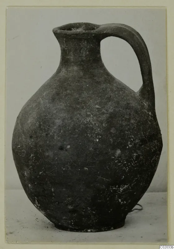 Plain pottery jug with a single handle, photographed against a pale background.