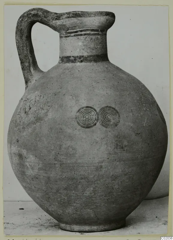Pottery jug with a high loop handle, banded neck and two concentric circle motifs on the body.