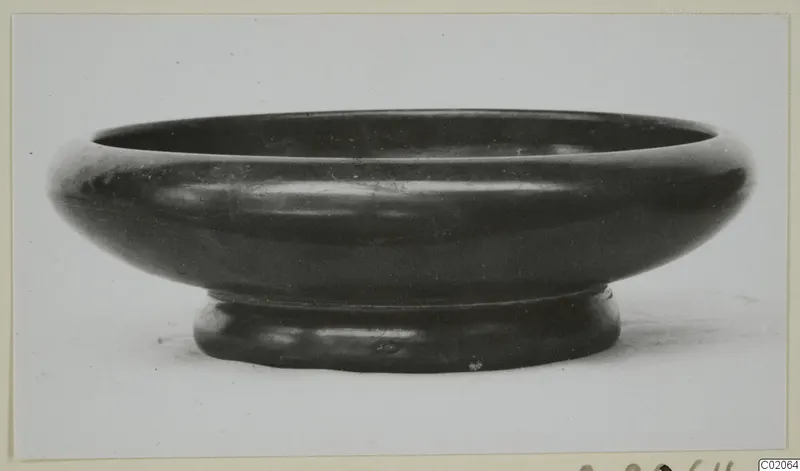Black Glazed Ware bowl with a wide rounded body and a short ring foot, seen from the side
