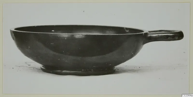 Black glazed bowl with a single horizontal handle, seen from the side.