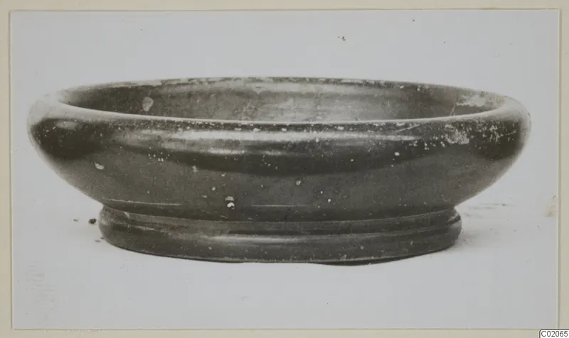 Black glazed ware bowl with a wide rounded body and ring foot, seen from the side.