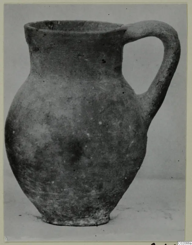 Pottery jug with a single loop handle, shown from the side against a plain grey backdrop.