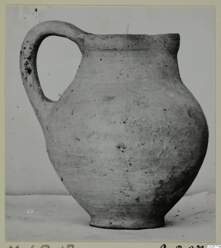 Pottery jug with a single loop handle and a wide globular body, photographed against a plain background.
