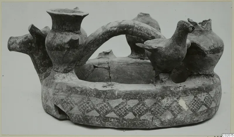 Pottery vessel with a ring-shaped base, painted triangle bands, a modelled bird and an animal head, photographed against a pale background