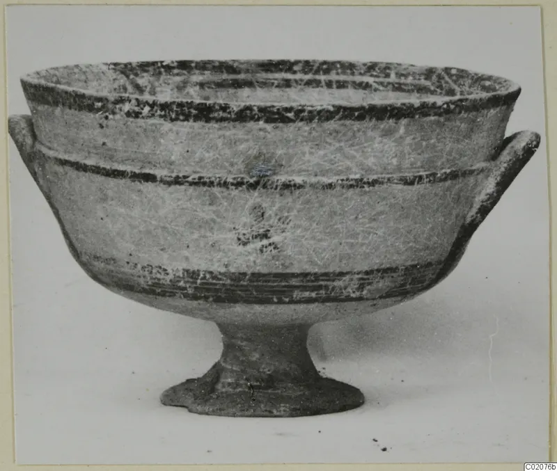 Pottery bowl on a stemmed foot with two horizontal handles, dark painted bands on a pale surface