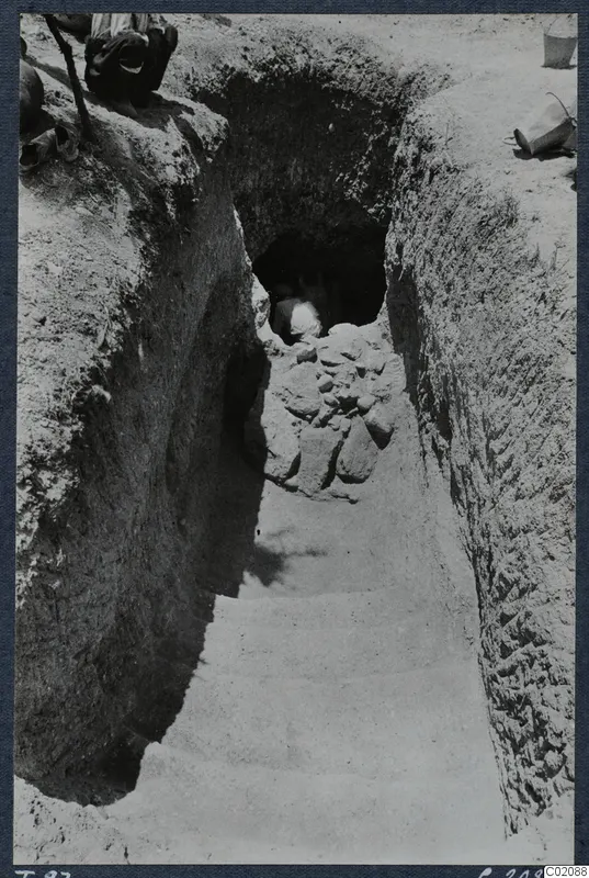 Sloping dromos leading down to a tomb entrance at Marion, with a person in the doorway and a bucket on the bank.