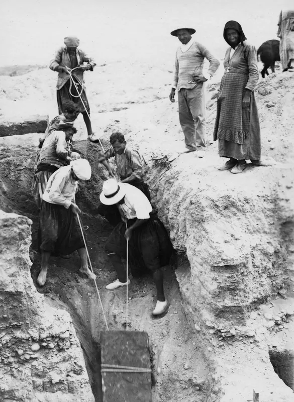 Workers pulling ropes to haul a wooden board up a narrow trench at Marion, with a man and woman watching from the edge.