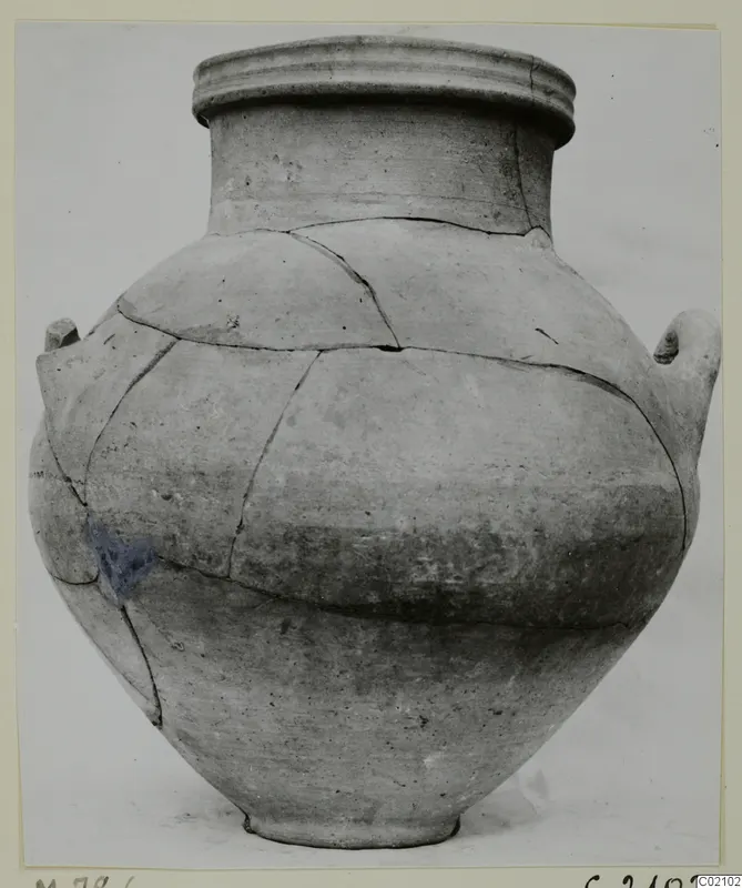 Large plain pottery vessel with a wide rim and two handles, cracked and pieced back together, against a pale background.