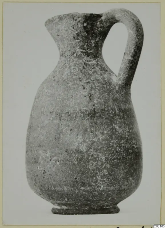 Pottery jug with a loop handle, flared mouth and ring foot, photographed against a plain pale background