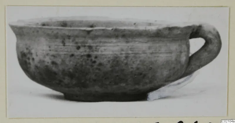 Pottery bowl with a single loop handle and a small foot, shown in profile against a white background