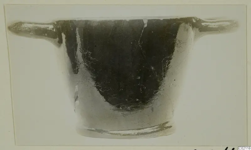 Black glazed pottery bowl with two horizontal handles and a low ring foot, seen from the side.
