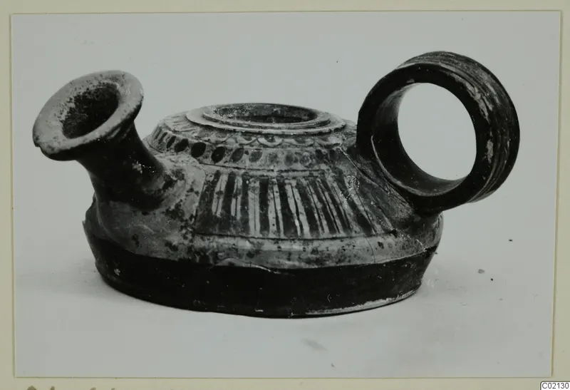Pottery oil lamp with a short spout, ring handle and striped shoulder, shown on a pale background