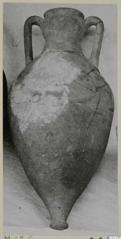 Two-handled pottery jar with a narrow neck and pointed base, pale surface with darker patches and cracks, against a grey backdrop.