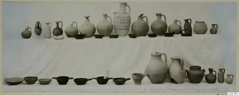 Pots and bowls from Tomb 25 at Marion, arranged in two rows on a white cloth.
