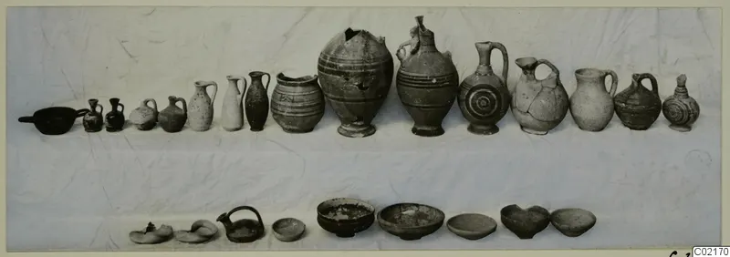 Pottery from Marion, Tomb 42: jugs, juglets, bowls and lamps laid out in two rows on a pale cloth